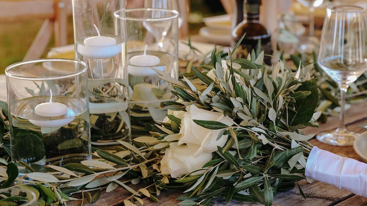 Tavolata con candele galleggianti, rami d'ulivo e rose bianche